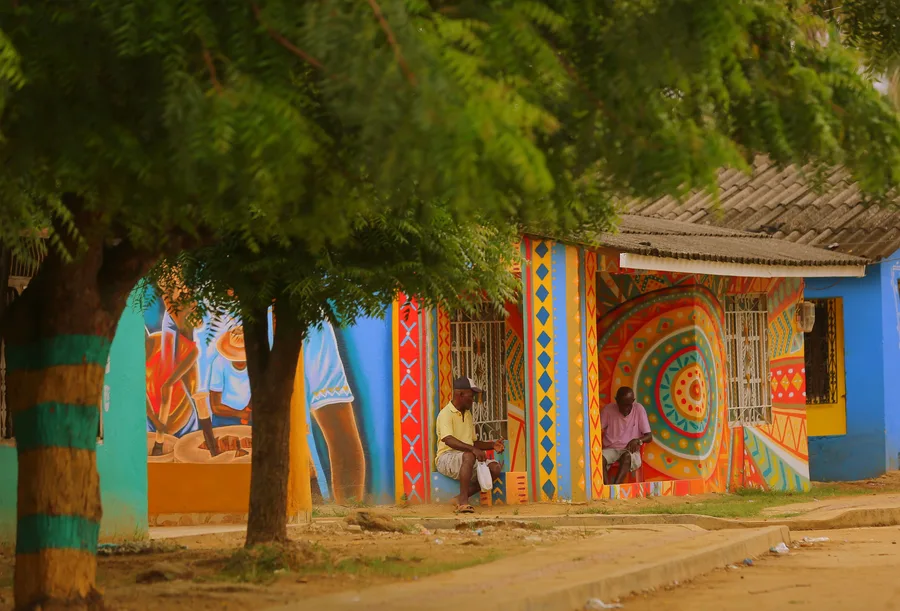 Mujeres con vestidos de colores bailando junto al letrero de San Basilio de Palenque
